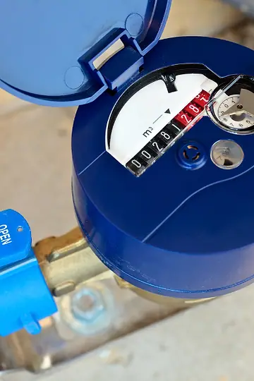 Hidrômetro azul instalado em cano de metal, com o mostrador aberto