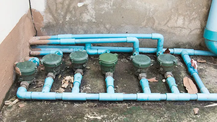 Fileira de hidrômetros verdes instalados em tubulação azul, no chão de um condomínio