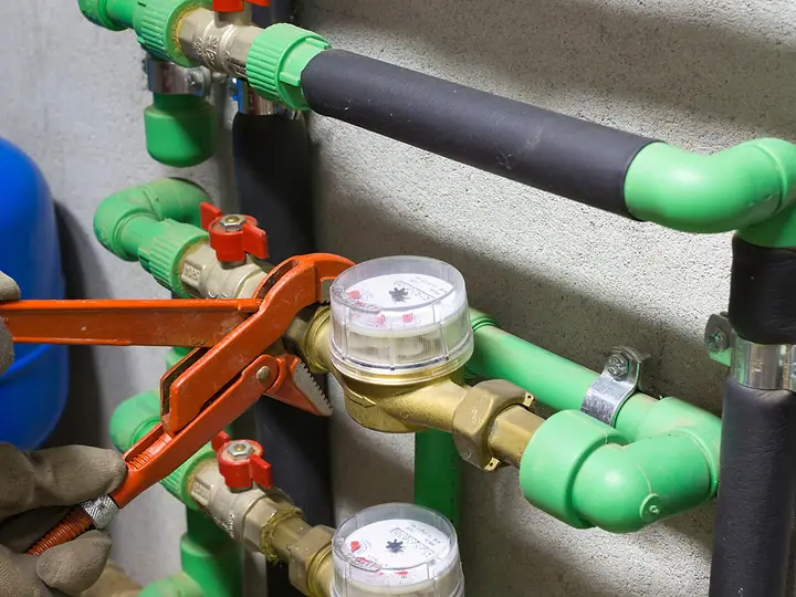 Encanador apertando com chave de grifo a conexão de um hidrômetro na tubulação verde