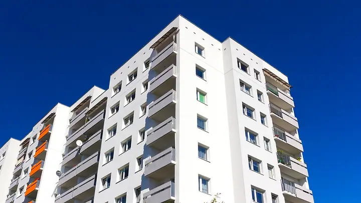 Fachada de prédio residencial branco com varandas, contra o céu azul