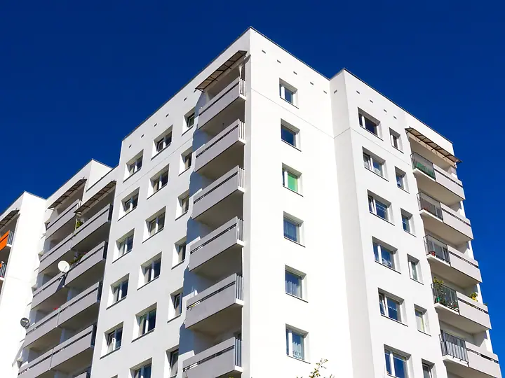 Fachada de prédio residencial branco com varandas, contra o céu azul